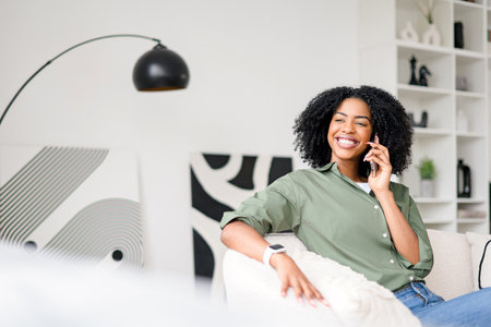 The woman relaxes on the couch, her contagious smile present as she enjoys a casual conversation over the phone, epitomizing the comfort and connection of mobile communicationの写真素材