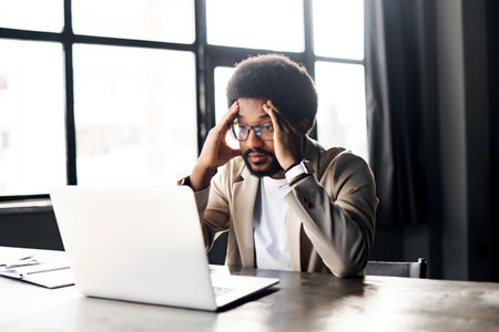 With a pensive expression Brazilian businessman contemplates his work on a laptop, embodying the...
