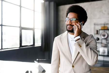 Young businessman is engaging happily on a phone call captured against the serene backdrop of an urban office. The photograph encapsulates a moment of pleasant business communicationの写真素材