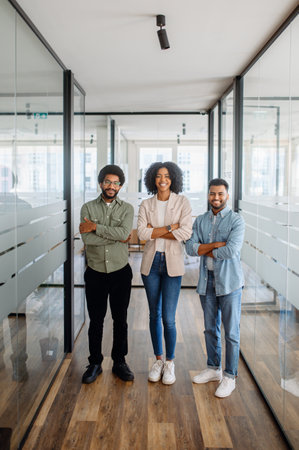 Three confident business professionals standing with arms crossed in a modern office. A symbol of teamwork, leadership, and corporate ambition.の写真素材