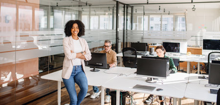 A confident female executive standing in a modern office while her team works in the background. A representation of leadership, business success, and professional empowerment.の写真素材