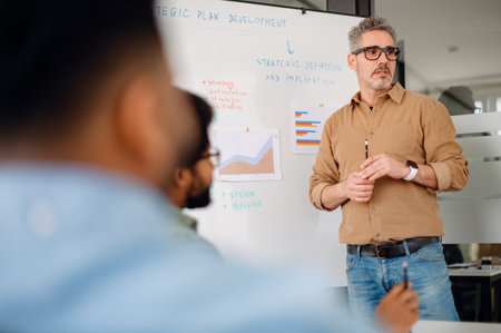 Business leader presenting strategic plans to a diverse team in a modern office. Engaged professionals discussing company growth, data-driven decision-making, and corporate success.の写真素材