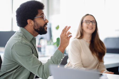 Smiling young professional confidently working in a creative office environment. Engaged in a collaborative discussion with a diverse team, bringing fresh ideas to the table.の写真素材