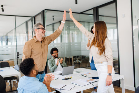 Energetic business professionals celebrate progress with a high-five, reinforcing the importance of teamwork and positivity in a thriving work environment.の写真素材