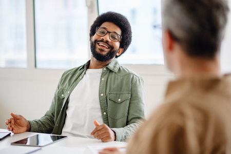 A young professional in a denim shirt smiling during a meeting in a bright office. The relaxed and friendly atmosphere enhances team collaborationの写真素材