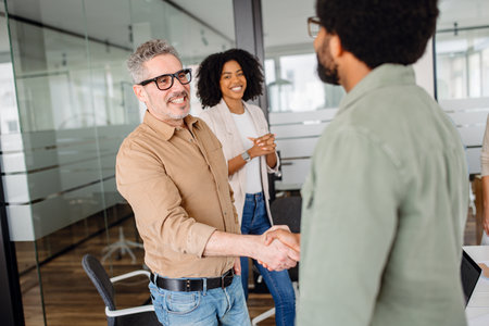 A professional handshake between two business colleagues in a modern office. Smiling coworkers observe, symbolizing agreement, teamwork, and successful partnership in a collaborative work environment.の写真素材