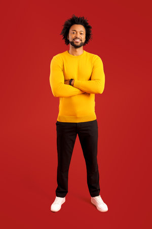 Portrait of happy satisfied handsome young man standing with crossed arms and looking at camera with...