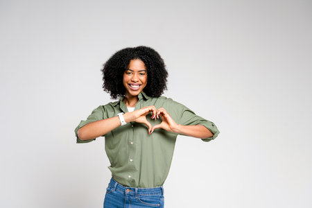 An exultant African-American woman now creates a heart shape with her hands, in a more dynamic and full-bodied pose. The concept of love and positivity is enhanced by her bright, engaging smileの写真素材