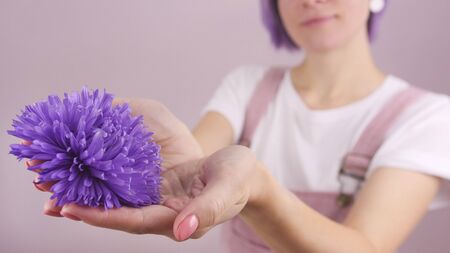 Purple flower in woman's hands on pink background, girl gives flowers, present