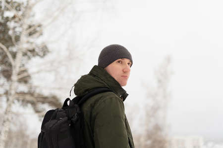 Pakren in a green jacket and with a backpack against the background of the winter landscape stands...