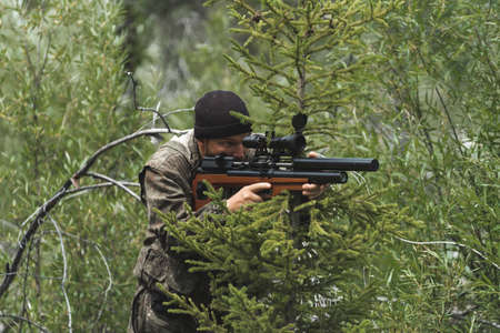 A man with a rifle sits in an ambush. The sniper is preparing to shoot.