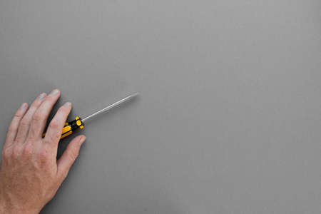 The hand holds the screwdriver against a gray background. space for textの写真素材