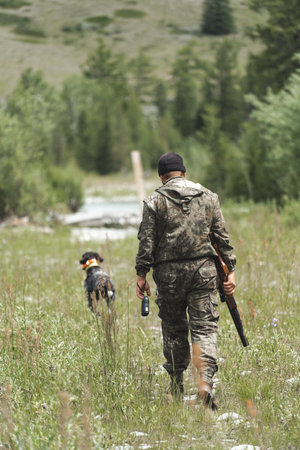 A hunter with a dog walks through a forest glade and holds a rifle in his hands.の写真素材