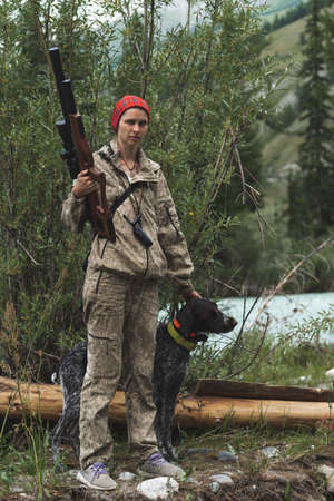 Female hunter in camouflage clothes ready to hunt, holding gun and walking in forest. hunting and people conceptの写真素材