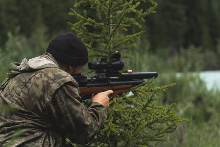The hunter aims with a rifle. A man in camouflage is preparing to shoot. Hunting in the woods with a sniper rifleの写真素材