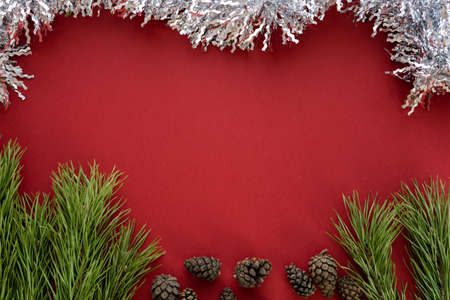 Christmas composition. Spruce branches and shishki with white tinsel on a red background. Flat lay, top view, space for textの写真素材