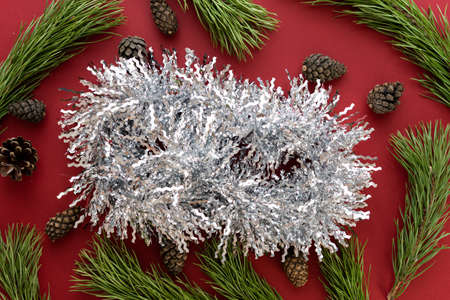 Christmas composition. Spruce branches and shishki with white tinsel on a red background. Flat lay, top view, space for textの写真素材