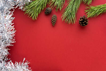 Christmas composition. Spruce branches and shishki with white tinsel on a red background. Flat lay, top view, space for textの写真素材