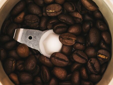 Grains of roasted coffee lie near a knife in a coffee grinderの写真素材