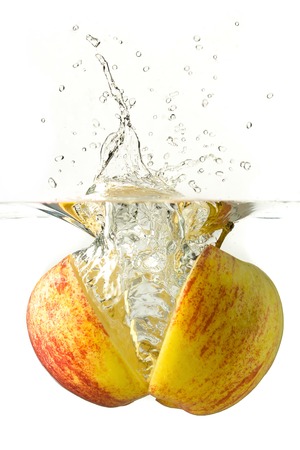 Ripe sliced apple falling into water, splashes all around.の写真素材