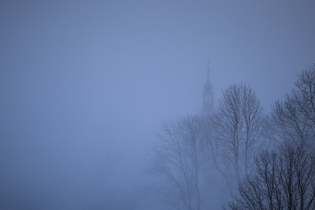 Small village with church and tree silhouette in a fogの写真素材