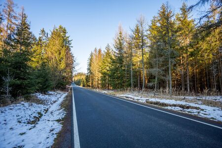 A wet roadway where a snow storm has left snow even on the bright colored leaves still in the trees lining the tarmac blacktop road during a europe winter. Simple road wallpaper.の写真素材