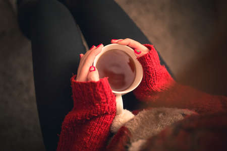 Top down shot of a Girl with a warming tea drink in hands sitting on the sofa with christmas colored fingernails and reindeer sweater.の写真素材