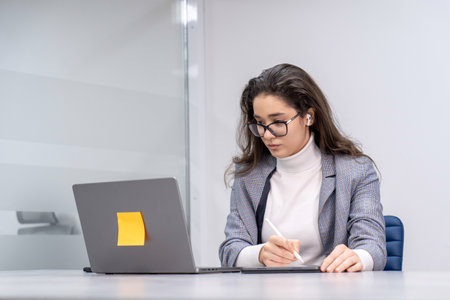 Young business woman participating in an online meeting and taking notes on her tablet.の写真素材