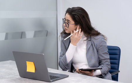 Young business woman adjusting the sound on her headphones while listening to a podcast and taking notes on her electronic tabletの写真素材