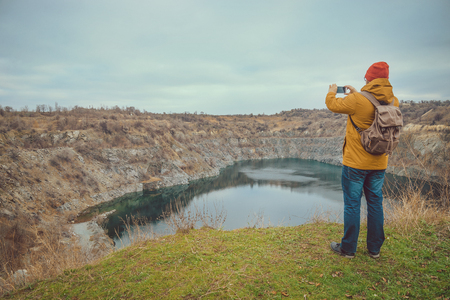 hipster guy taking photo on his mobile phone camera of lake in cold autumn dayの写真素材