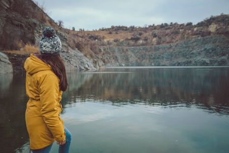 Woman in boots and jeans walks along the lake shore in autumn career