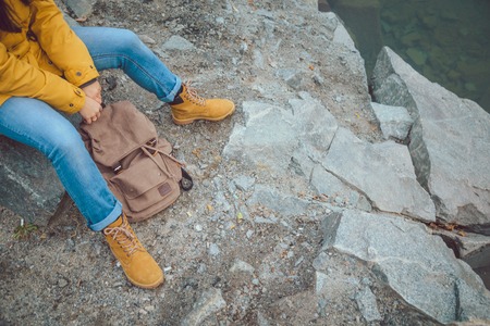 Female legs in jeans and hiking boots near edge of mountain lake. Rocks reflection on water surfaceの写真素材