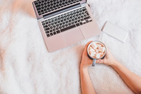 woman drinking coffee at home in her bed while checking her laptopの写真素材