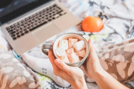 woman drinking coffee at home in her bed while checking her laptop