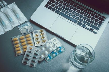 pills near laptop with glass of waterの写真素材