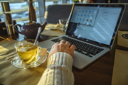 male sitiing in caffe drinking tea and working on laptop