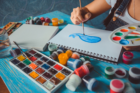Pretty smiling young woman drawing a picture with poster paintの写真素材
