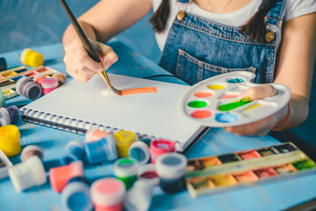 Pretty smiling young woman drawing a picture with poster paintの写真素材