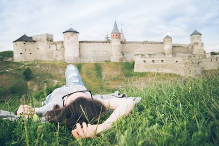 young pretty woman lie in fron of old castleの写真素材