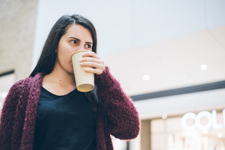 Young woman with smart phone and cup of coffee standing near cafeの写真素材