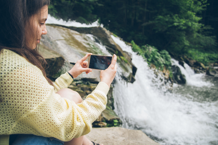 woman taking picture on the phone of waterfall on backgroundの写真素材