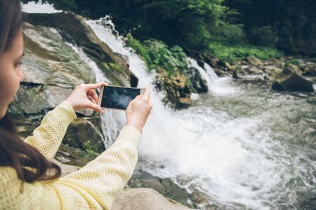 woman taking picture on the phone of waterfall on backgroundの写真素材