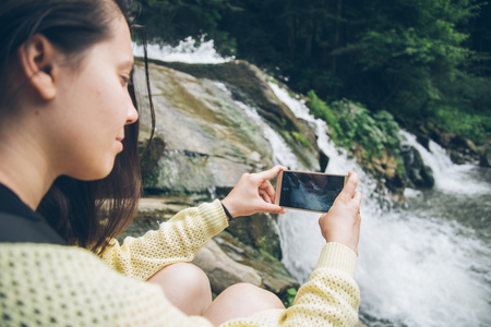 woman taking picture on the phone of waterfall on backgroundの写真素材