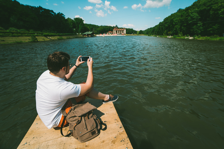 Man sitting on a lake pier and taking picture on the phoneの写真素材