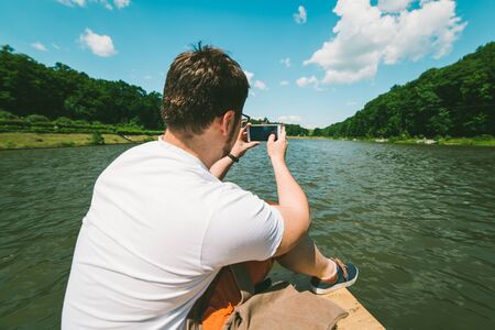 Man sitting on a lake pier and taking picture on the phoneの写真素材