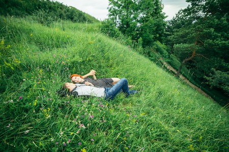 Young happy beautiful couple man and woman lying outdoors on the bright sunny day on green lawnの写真素材