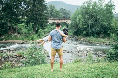 man taking woman on his arms near mountains riverの写真素材