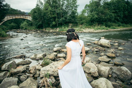 woman standing near mountains river in white dress and looking at the viewの写真素材