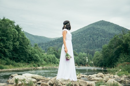 woman standing near mountains river in white dress and looking at the viewの写真素材