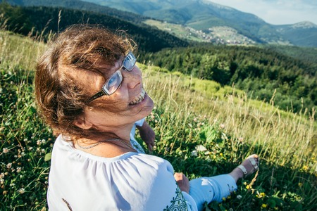 mature woman sitting on the peak of the hill and enjoing the viewの写真素材
